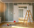 Ladder, red paint, and roller in a living room are being renovated.