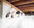 Person in protective gear installing a crawl space vapor barrier with plastic sheeting under a house.