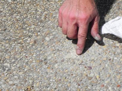 Hand pointing at a small hole in a concrete surface with a tissue nearby.