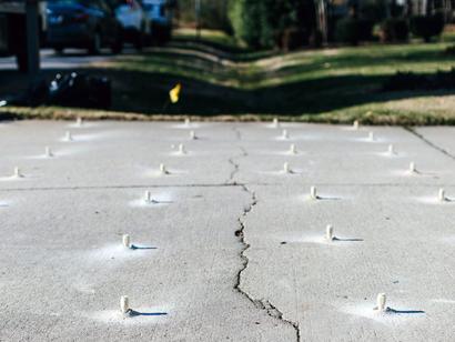 Concrete surface with visible crack and white plastic plugs inserted in a grid pattern.