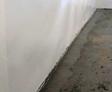 Freshly plastered wall with a bare concrete floor in a room under renovation, perfect for starting basement cleaning projects.