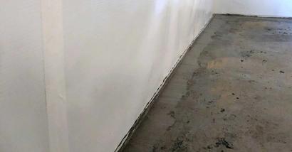 Freshly plastered wall with a bare concrete floor in a room under renovation, perfect for starting basement cleaning projects.