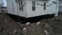 A house is raised off the ground with visible foundation work and dirt piled around.