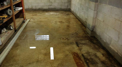 A cluttered workshop with water pooling on the stained concrete floor.