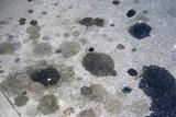 Concrete surface with various dark oil stains scattered across.