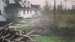 Abandoned house with boarded windows, overgrown bushes, and wooden debris in the foreground.
