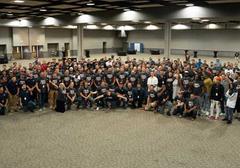 A large group of people in matching shirts gathers in a spacious hall for a group photo.