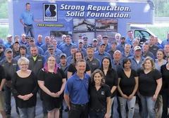 Group photo of a company team standing in front of a branded van with "Strong Reputation. Solid Foundation." slogan.
