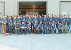A group of people wearing matching shirts pose in front of a garage with a "Foundation" sign.