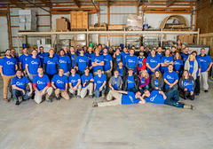 A large group of people in blue shirts posing together inside a warehouse.