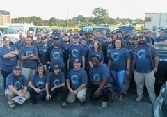 A large group of people wearing matching blue shirts, posing outdoors in a parking lot.