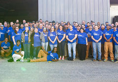 A large group of people in matching blue shirts pose for a group photo in front of a building.