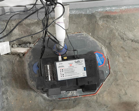 Basement sump pump securely installed in a sump pit with a SafeDri battery backup system on a concrete floor.