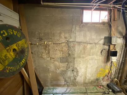 Cracked concrete wall in a dimly lit basement with exposed wires and a small window.