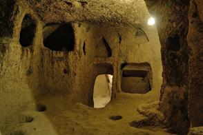 Underground cave with rough stone walls, small alcoves, and arched passageways dimly lit from above.