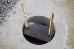 Circular concrete base with two vertical anchor bolts secured by a metal plate, surrounded by gravel.