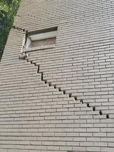 A brick wall with a diagonal crack pattern, often indicating potential foundation cracks, runs from a window down to the lower right side.