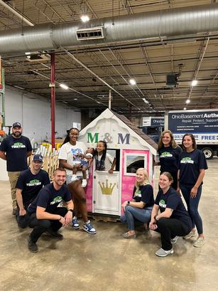 A group of people posing with a painted playhouse inside a large warehouse.