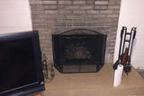 Fireplace with a metal screen harboring traces of creosote, TV on the left, and a roll of paper towels on the right.