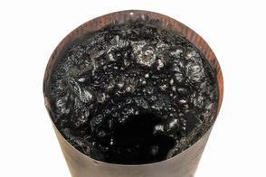 A barrel filled with thick, black creosote sludge on a white background.