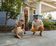 Three people inspect a large crack on the driveway in front of a house.