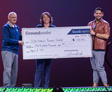 Three people holding a large check for $100,000 on stage.