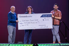 Three people holding a large check for $100,000 on stage.