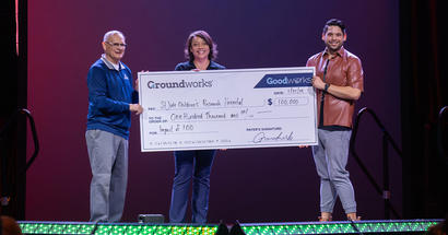Three people holding a large check for $100,000 on stage.