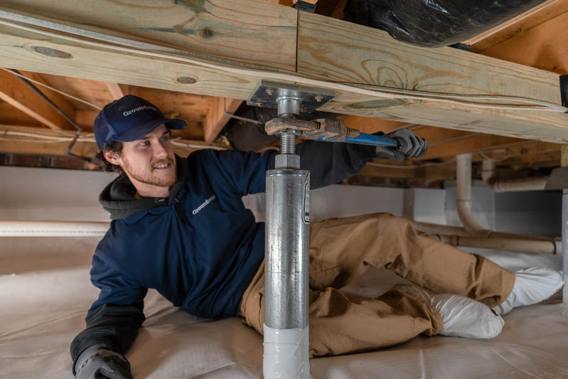 Person in work clothes adjusting a metal support beam under a wooden structure.