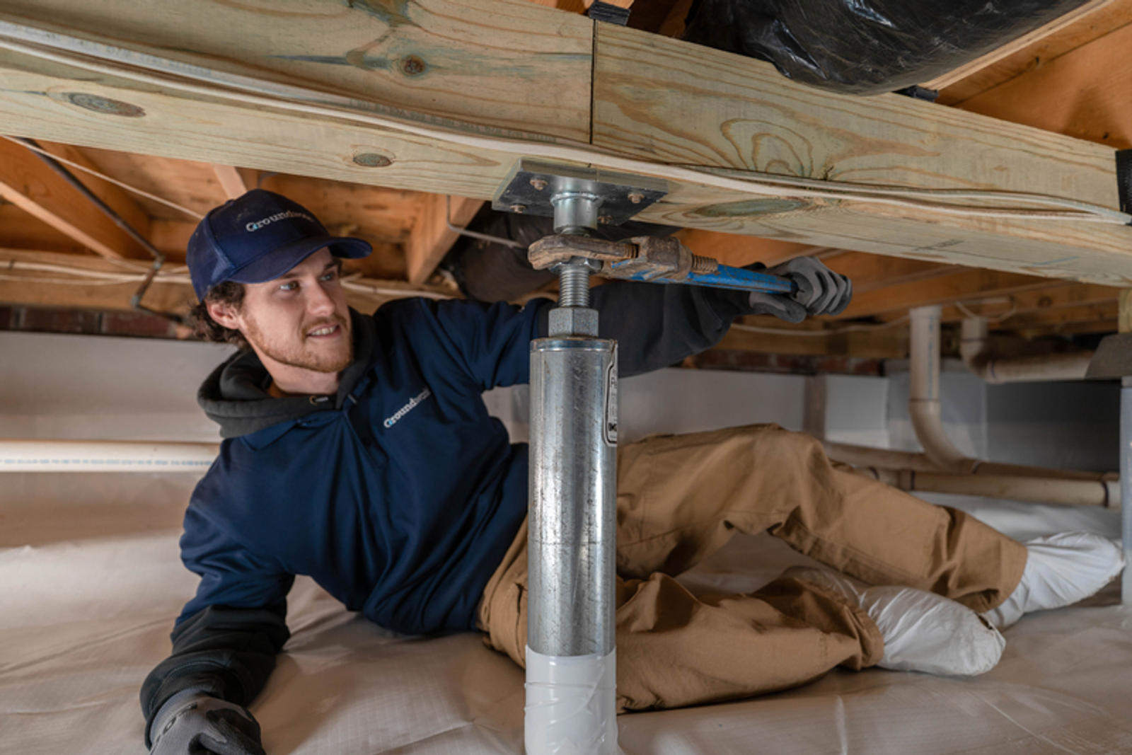 Person in work clothes adjusting a metal support beam under a wooden structure.