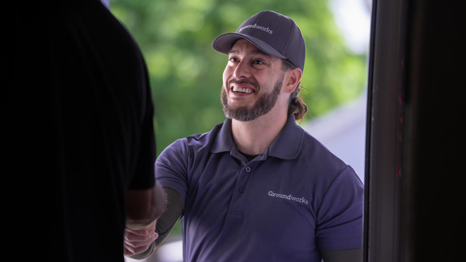 A man in a gray uniform and cap smiles while shaking hands with someone indoors.