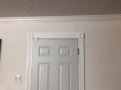 A door with ornate trim and a visible ceiling crack above in a white-walled room.