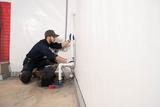 A plumber in uniform kneels by a wall, installing or repairing white pipes with tools nearby.