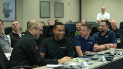 Group of people sitting at tables, smiling and engaged in a meeting or presentation.