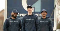Three workers in matching "Groundworks" hoodies and hats standing in front of a truck, smiling.