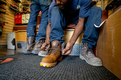 Two people trying on rugged work boots in a store, with one person lacing up a new brown boot.