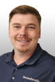 A man with short hair and a goatee smiles, wearing a navy blue shirt with the word "Groundworks" embroidered on it.