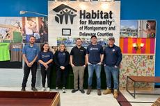 Six people standing in front of a Habitat for Humanity sign inside a building.