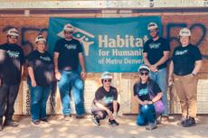 A group of volunteers wearing hard hats poses in front of a Habitat for Humanity sign.