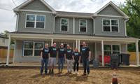 Six people in matching shirts stand in front of a two-story house under construction.
