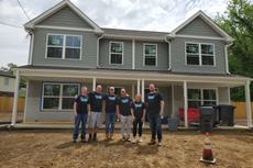 Six people in matching shirts stand in front of a two-story house under construction.