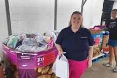 A smiling woman holding a white bag stands next to a bin filled with school supply packs.