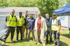 A group of seven men in work attire and safety vests stands proudly on the grass, smiling at the camera, reminiscent of a scene from one of Mike Rowe's worksite visits.