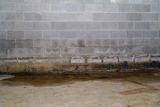Damp concrete basement wall with water stains and foundation water damage visible along the bottom edge.