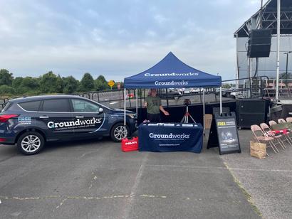 Groundworks booth with branded tent and car at an outdoor event, featuring promotional items on a table.