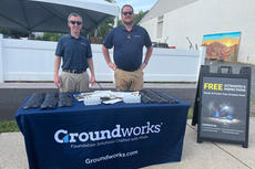 Two people at a booth with a "Groundworks" tablecloth, promotional items, and a sign offering free estimates and inspections.