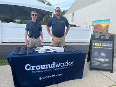 Two people at a booth with a "Groundworks" tablecloth, promotional items, and a sign offering free estimates and inspections.