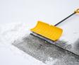 Yellow snow shovel clearing snow from concrete pavement.