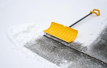 Yellow snow shovel clearing snow from concrete pavement.