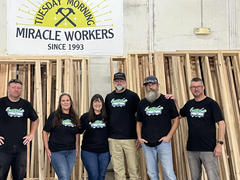 Group of six people wearing matching shirts, standing under a sign that says "Tuesday Morning Miracle Workers Since 1993.